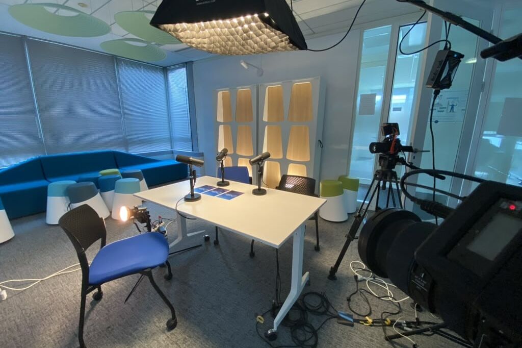 Plateau de tournage de podcast vidéo configuré dans une salle de réunion avec table, microphones Shure, softbox Godox, projecteurs et caméras sur trépied.
